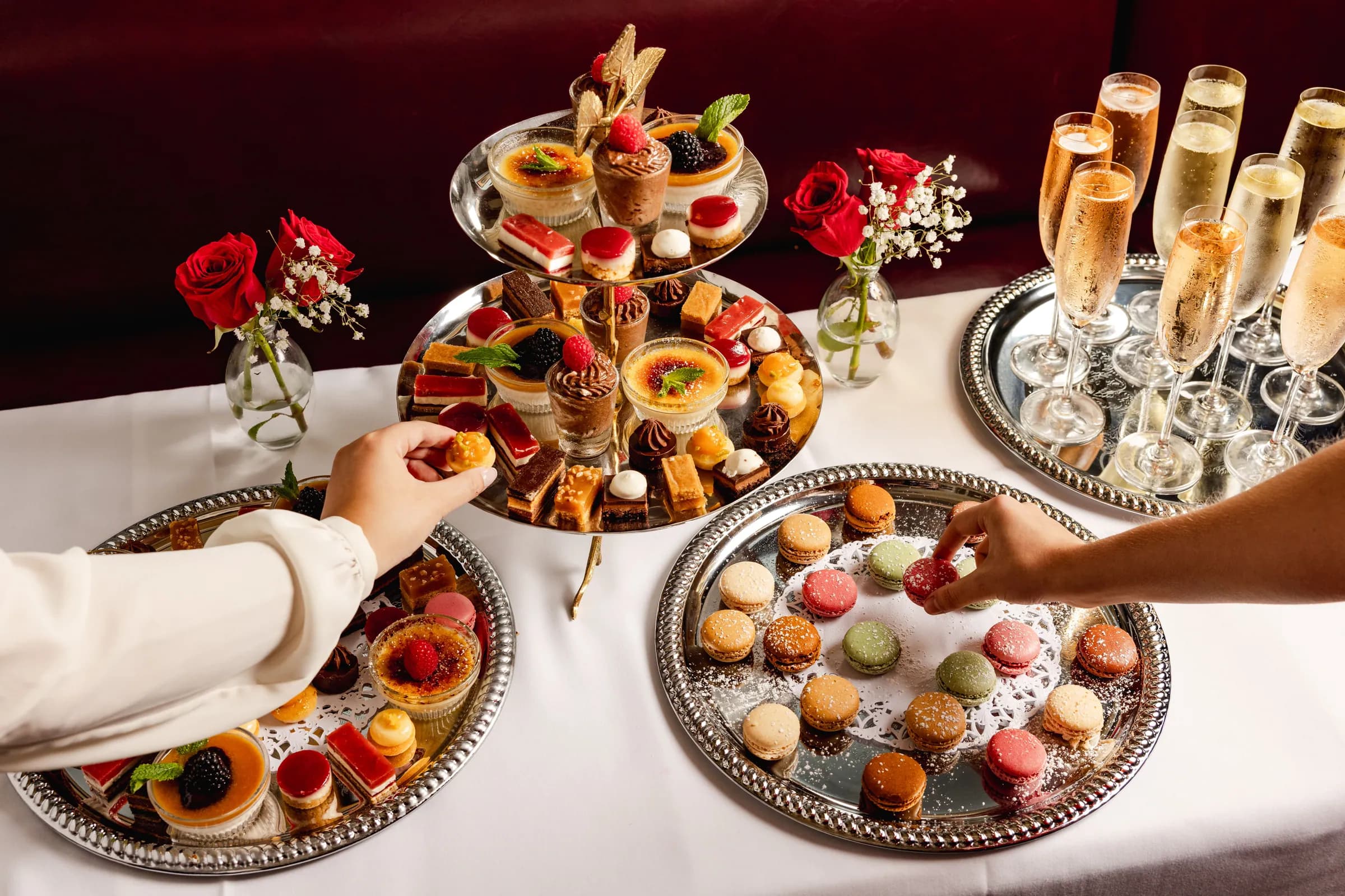 Guests reaching for macarons and pastries from a tiered stand, champagne alongside